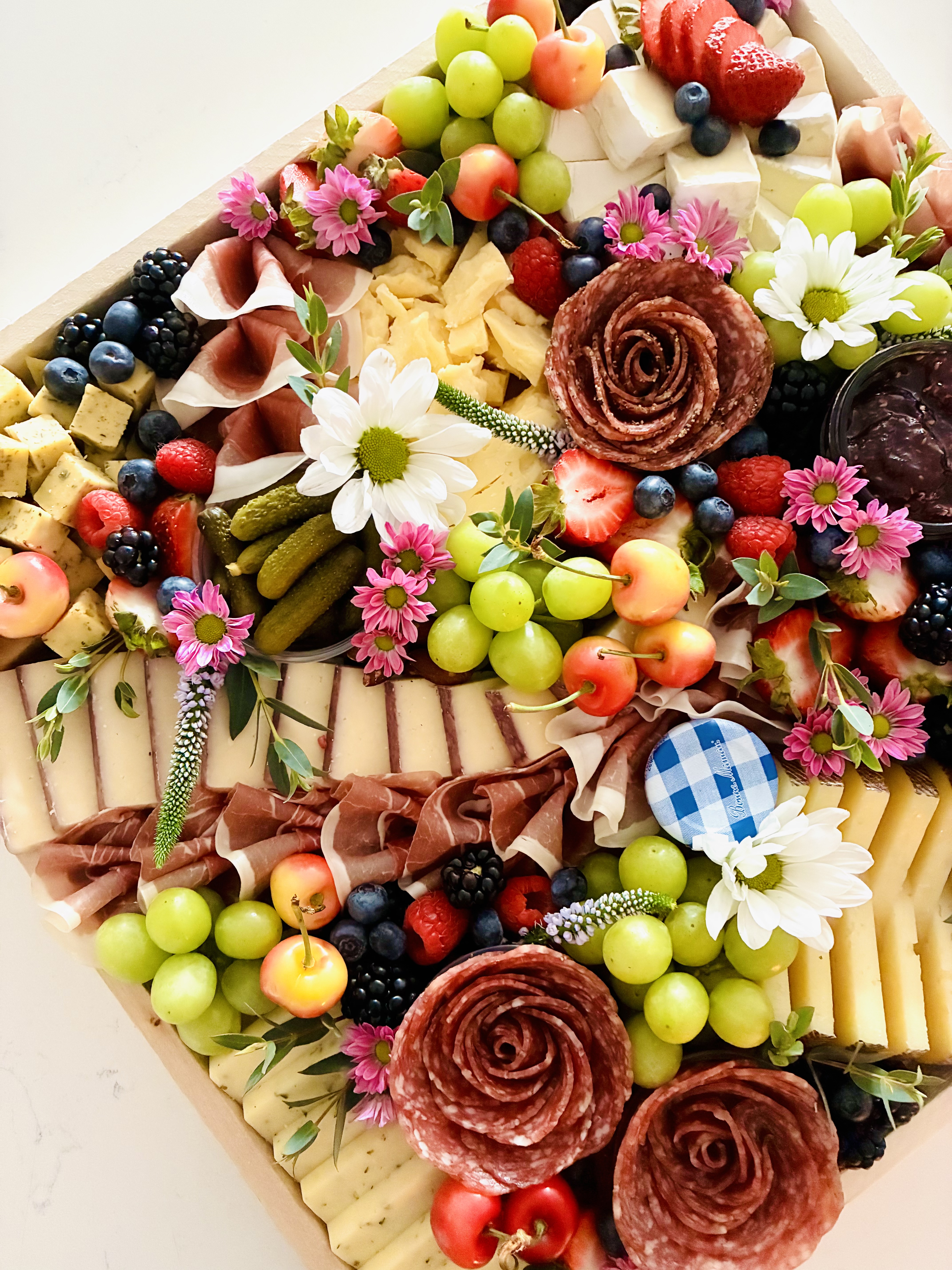 Botanically inspired cheese and charcuterie board with artisan cheeses, cured meats, seasonal fruit, and fresh florals by CharcuterieBrie.
