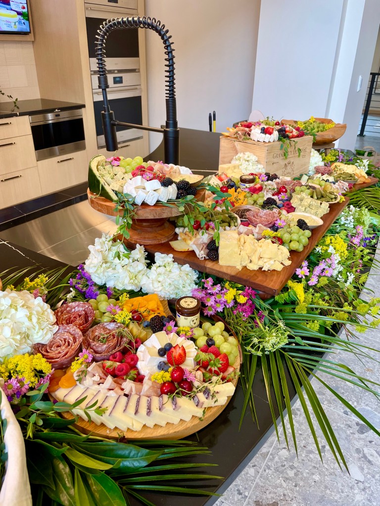 Luxury grazing table with multi-level layers of artisan cheeses, charcuterie, and seasonal fruit, accented with florals and greenery for events in Chicago and La Grange