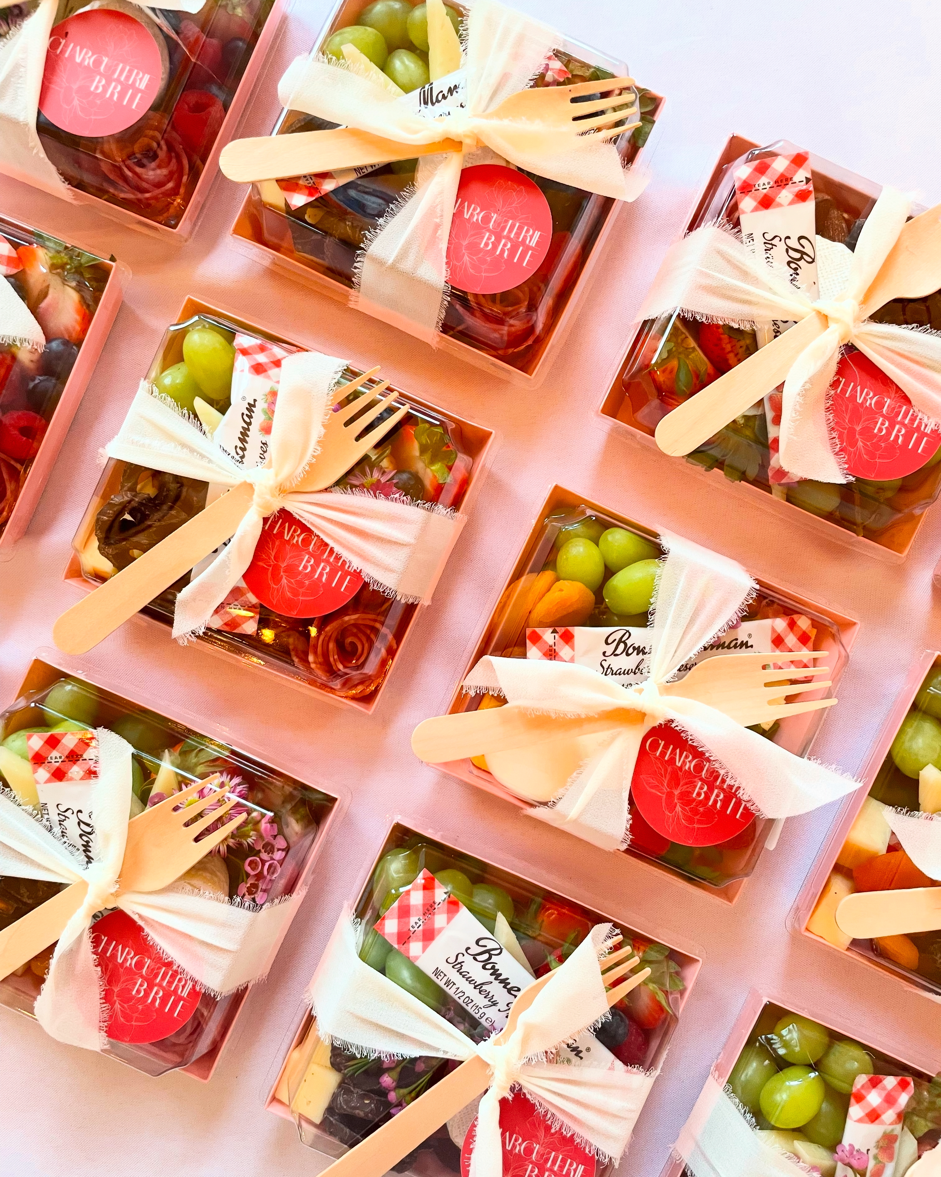Charcuterie box with three artisanal cheeses, salami, fresh fruit, roasted nuts, cornichons, Bonne Maman jam, and crackers, beautifully arranged for individual grazing