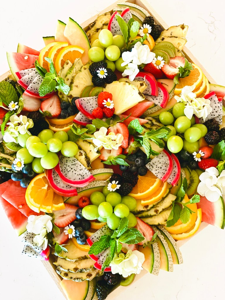 Artfully arranged fresh fruit board with seasonal fruits, berries, and botanical garnishes