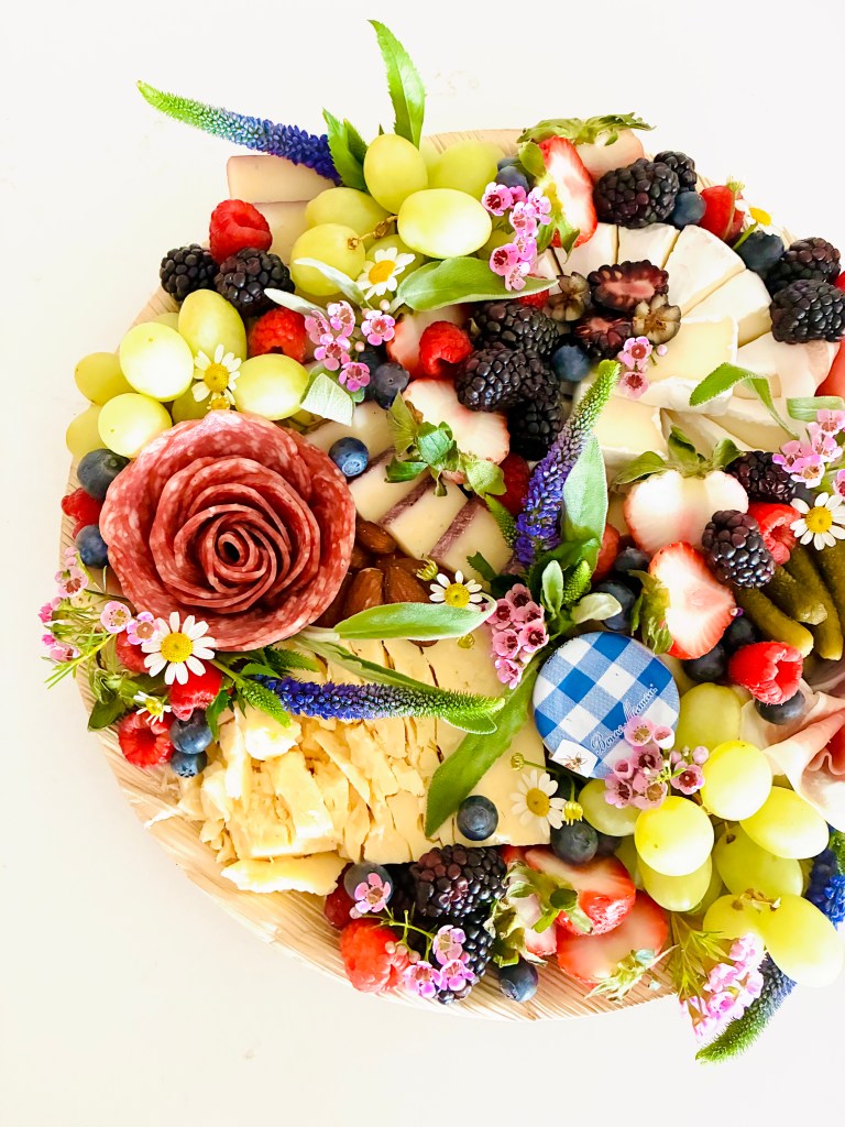 Petite cheese and charcuterie board with artisan cheeses, cured meats, fresh fruit, nuts, and botanical garnishes